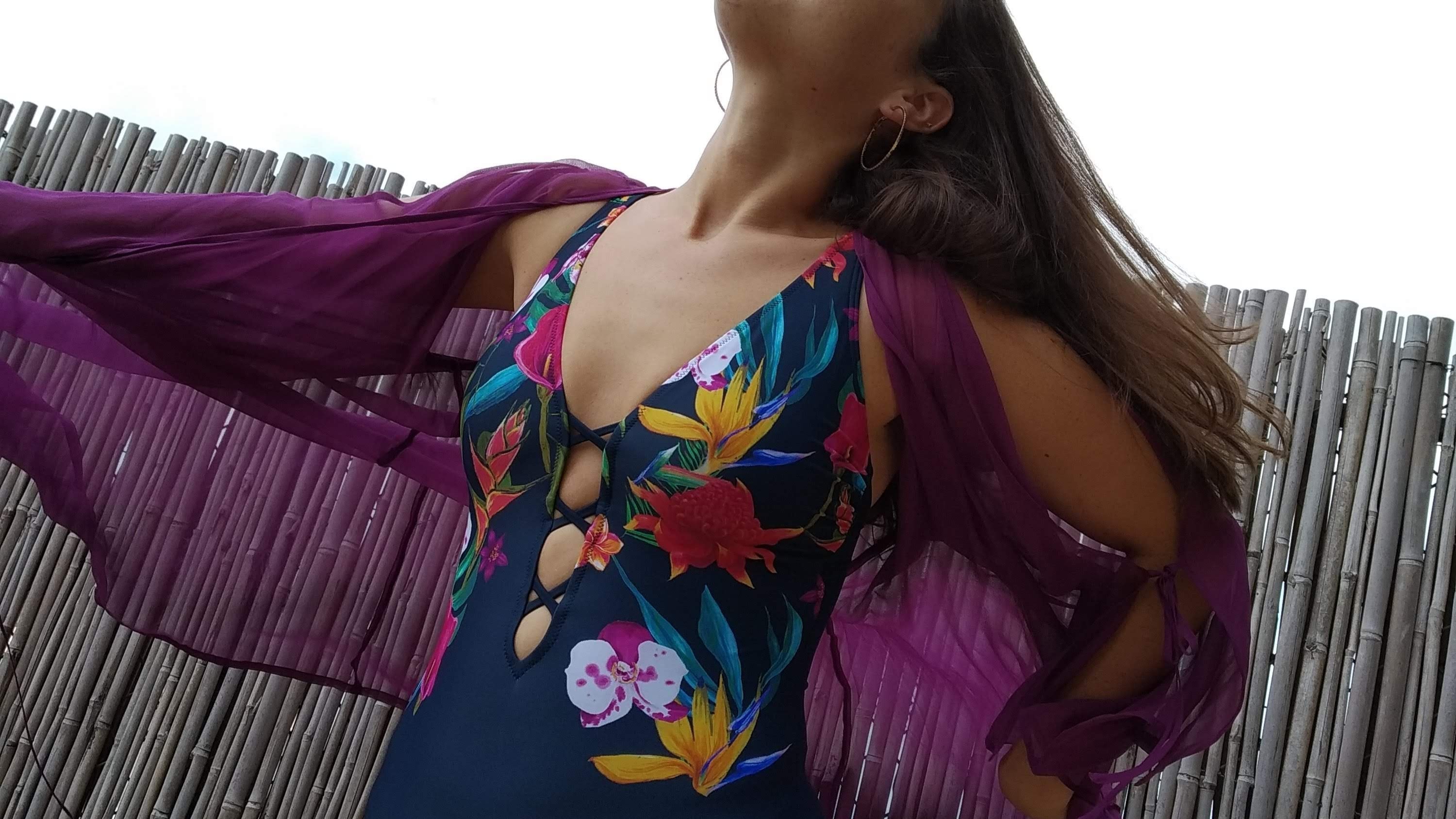 close up on a woman wearing a one piece swimming suit with flower print , and a purple cover-up.  אישה לובשת בגד ים פרחוני שלם עם עליונית סגולה