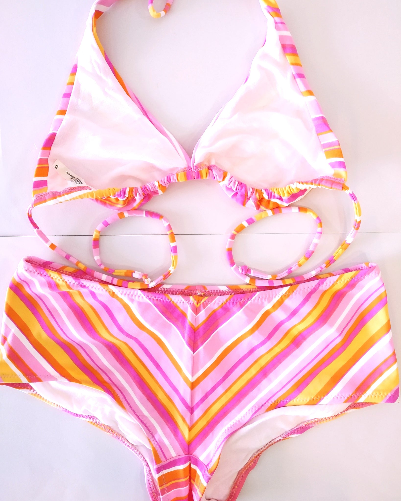 bikini set pastel-colored stripes pattern with large size of shorty bikini bottom and triangle halter bikini bra, with a short stretchy pink pareo spread on white background