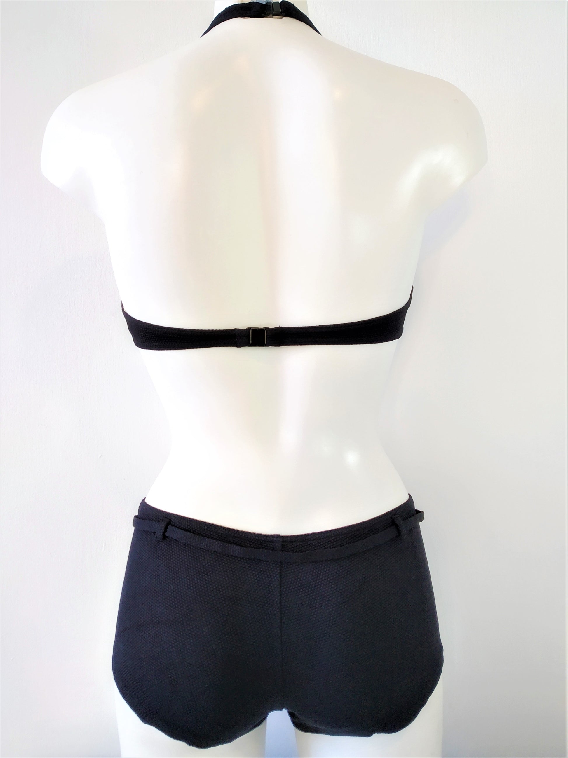 Back view of Two-piece black swimsuit, halter bra embellished with a black metal ring and low shorty bottom, black bikini. bikinn.com