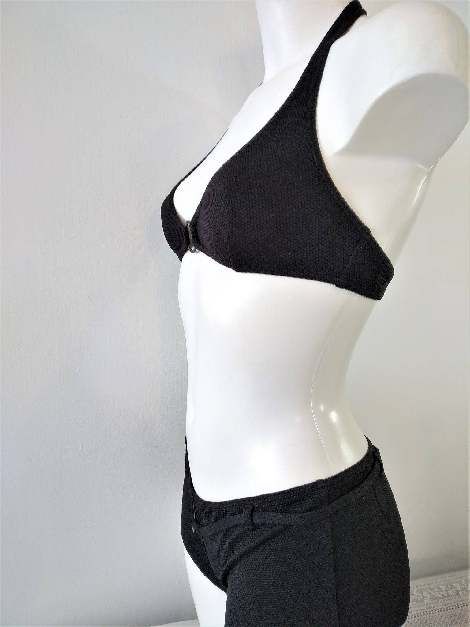 side view of Two-piece black swimsuit, halter bra embellished with a black metal ring and low shorty bottom, black bikini. bikinn.com