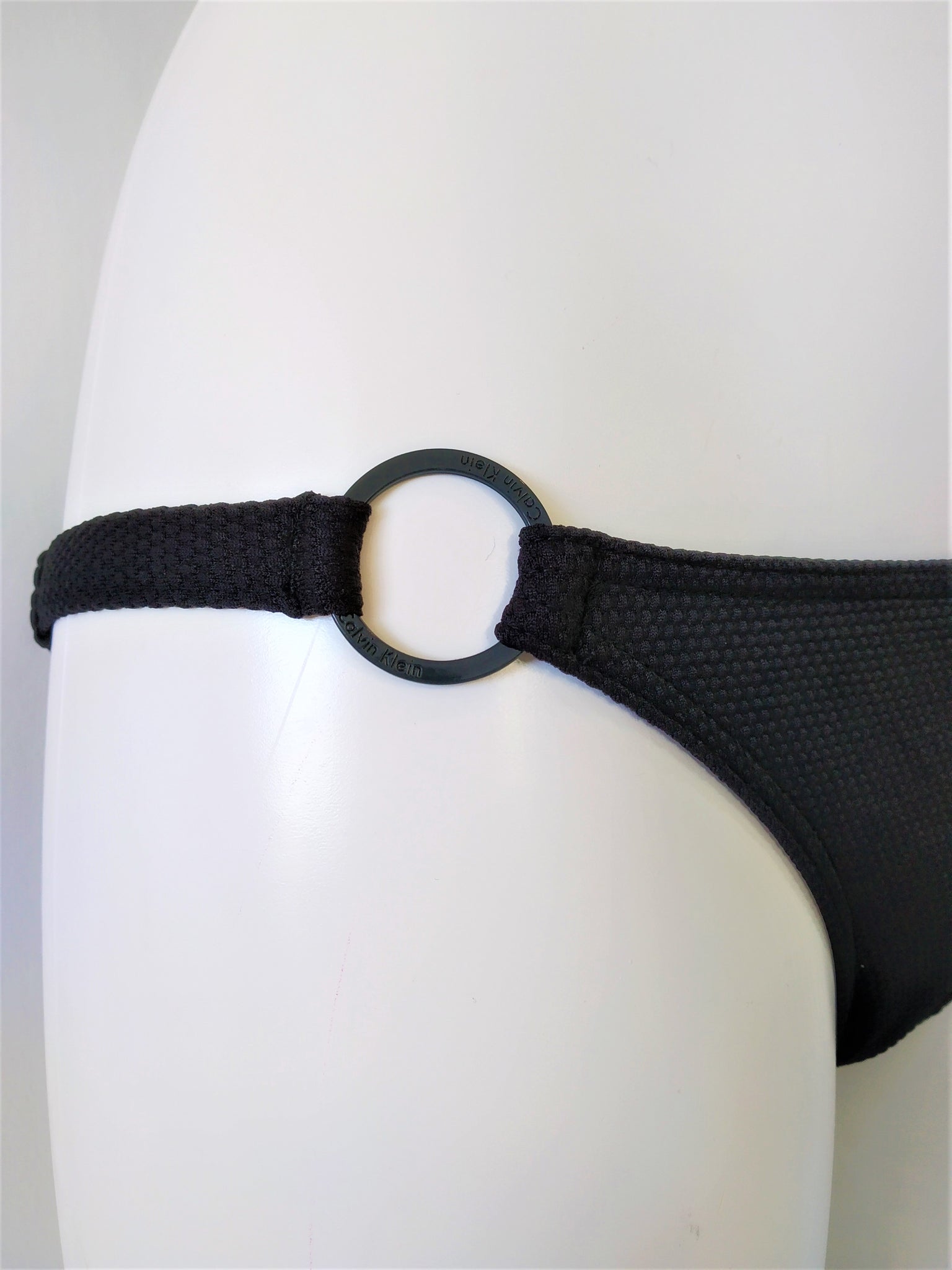 detail of side view of the bottom from the black bikini set, strapless lightly padded bra, regular bikini bottom, embellished with one flat black ring on each sides. bikinn.com