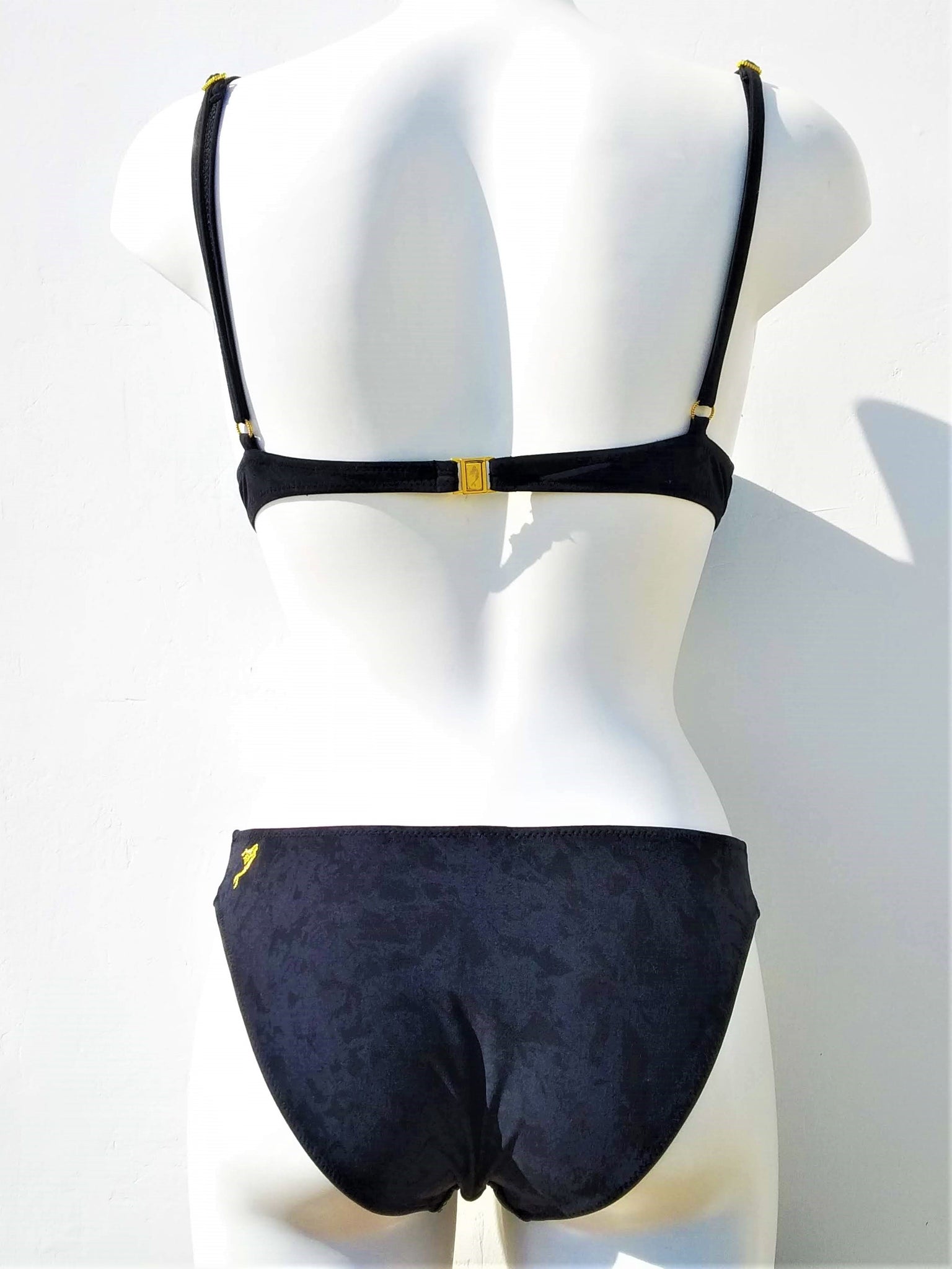 Back view of  Black bikini with double push-up bra, spaghetti straps and regular black bottom, with little mermaid embroidered in gold thread, as logo, on the side of the back band of the bra, and on the side of the back of the panties.. bikinn.com