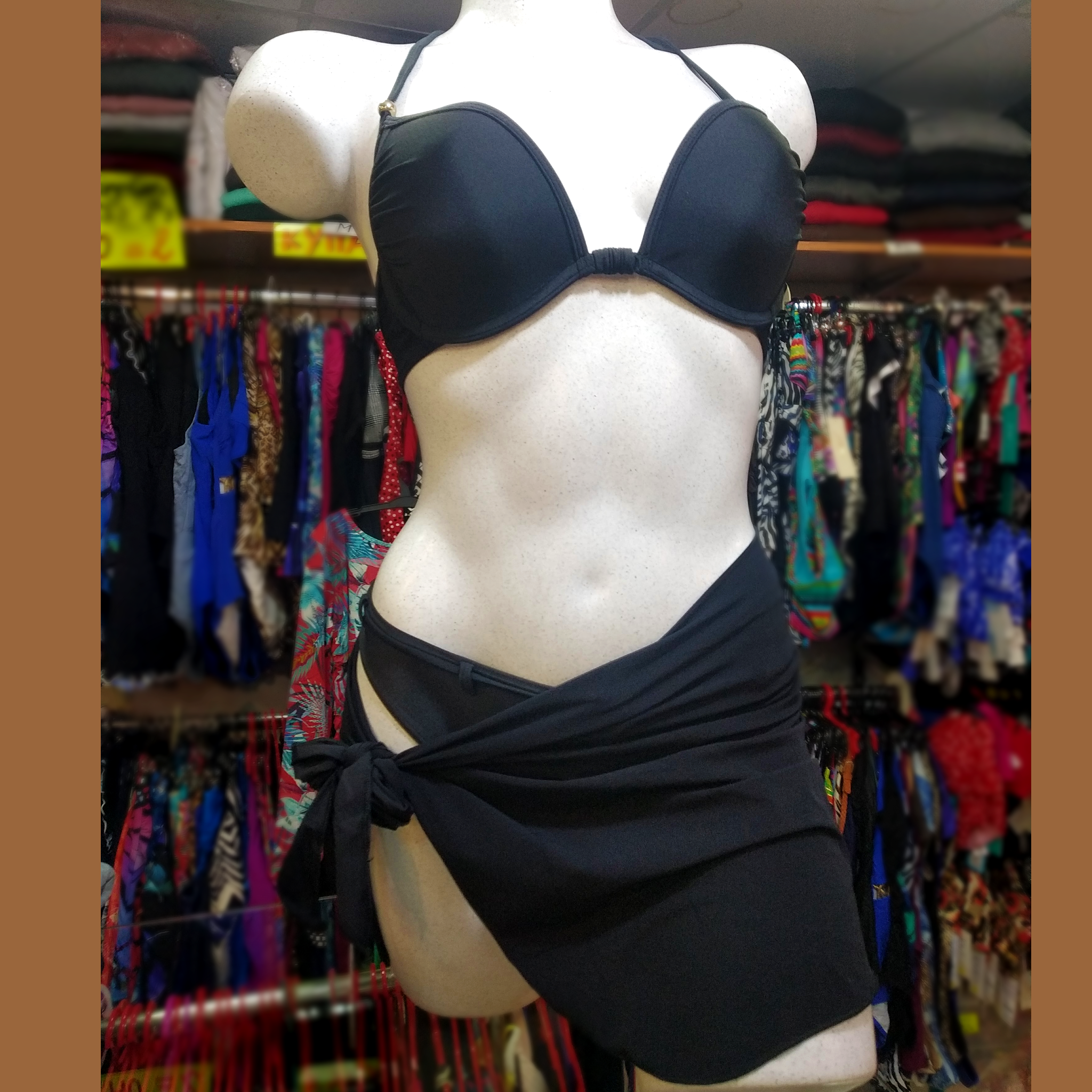 Black mini stretchy pareo tied around a white mannequin wearing a black push-up bikini set. 