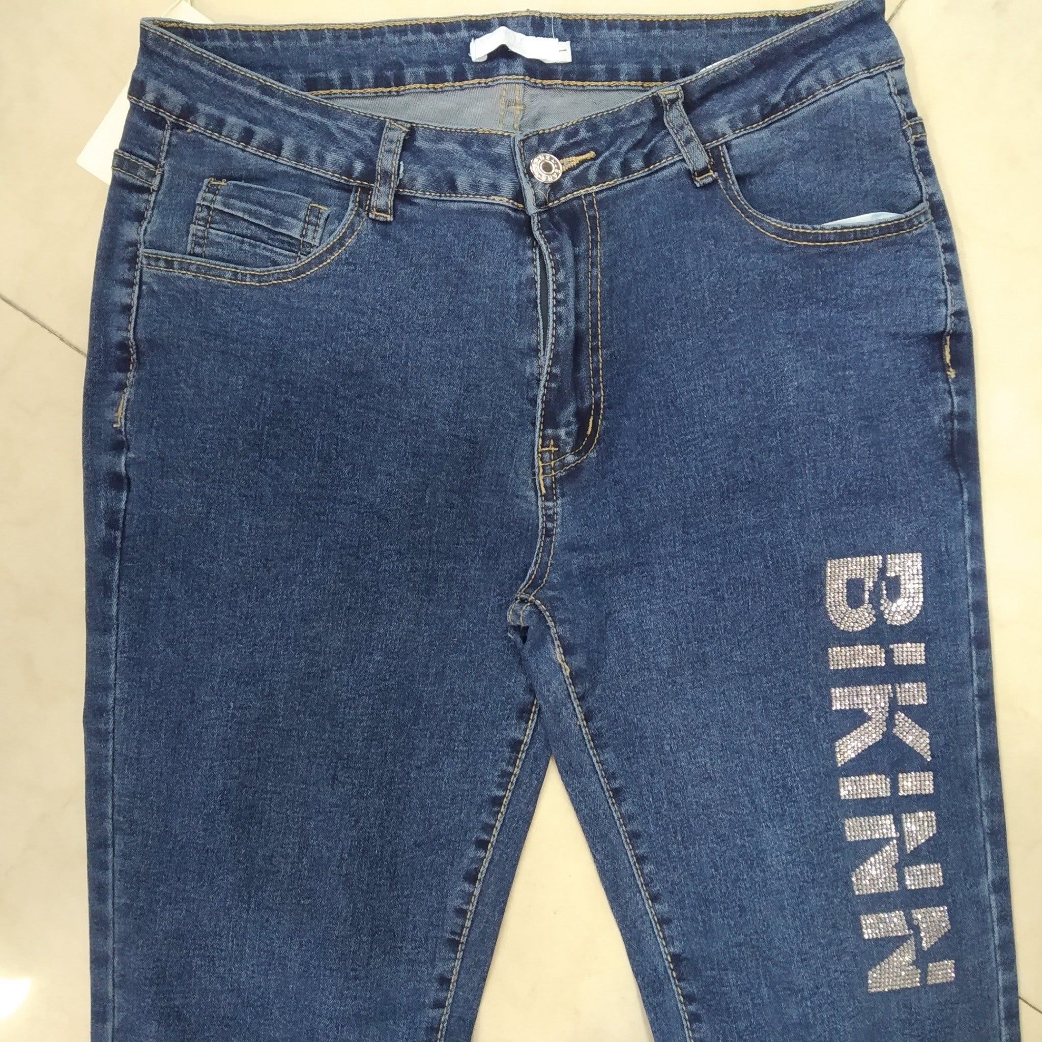 close-up view of the front of a skinny strech jeans on the floor  with a sparkling diamond logo printed on the thigh. bikinn.com